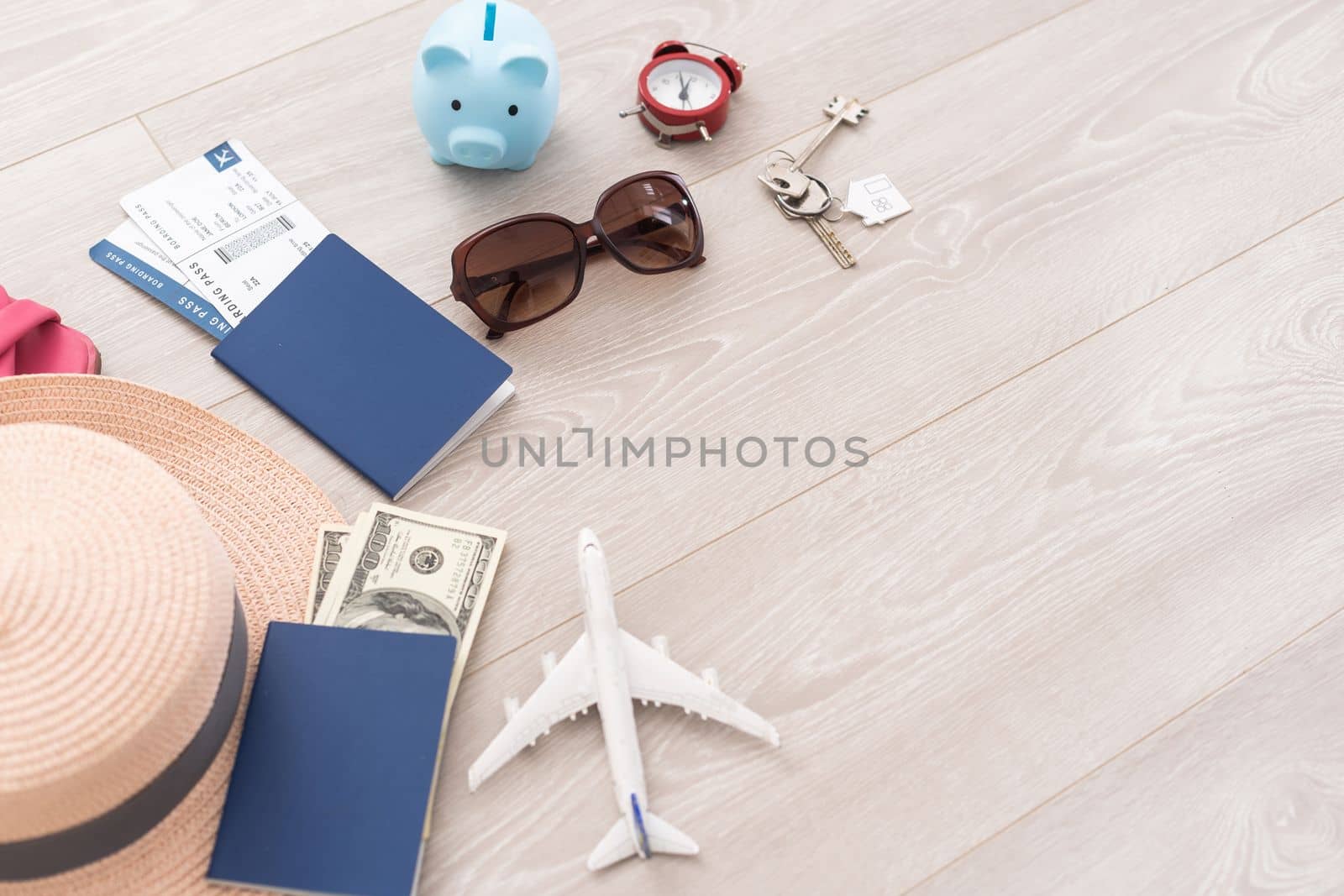 Pink piggy bank, straw hat, money, passport and sunglasses on wooden table.