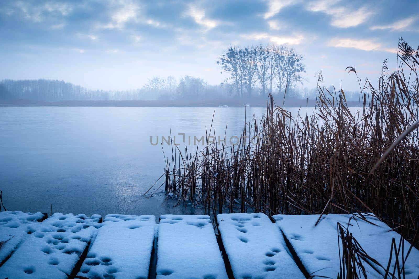A snow-covered pier and a frozen, misty lake, winter nature landscape