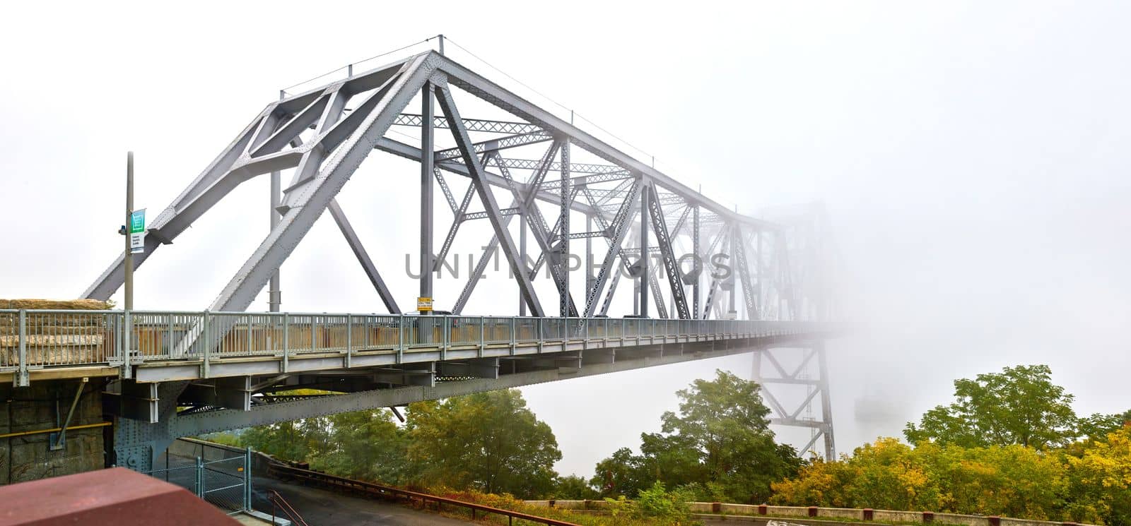 Panorama of full steel bridge in New York fading away into fog on foggy weather morning by njproductions