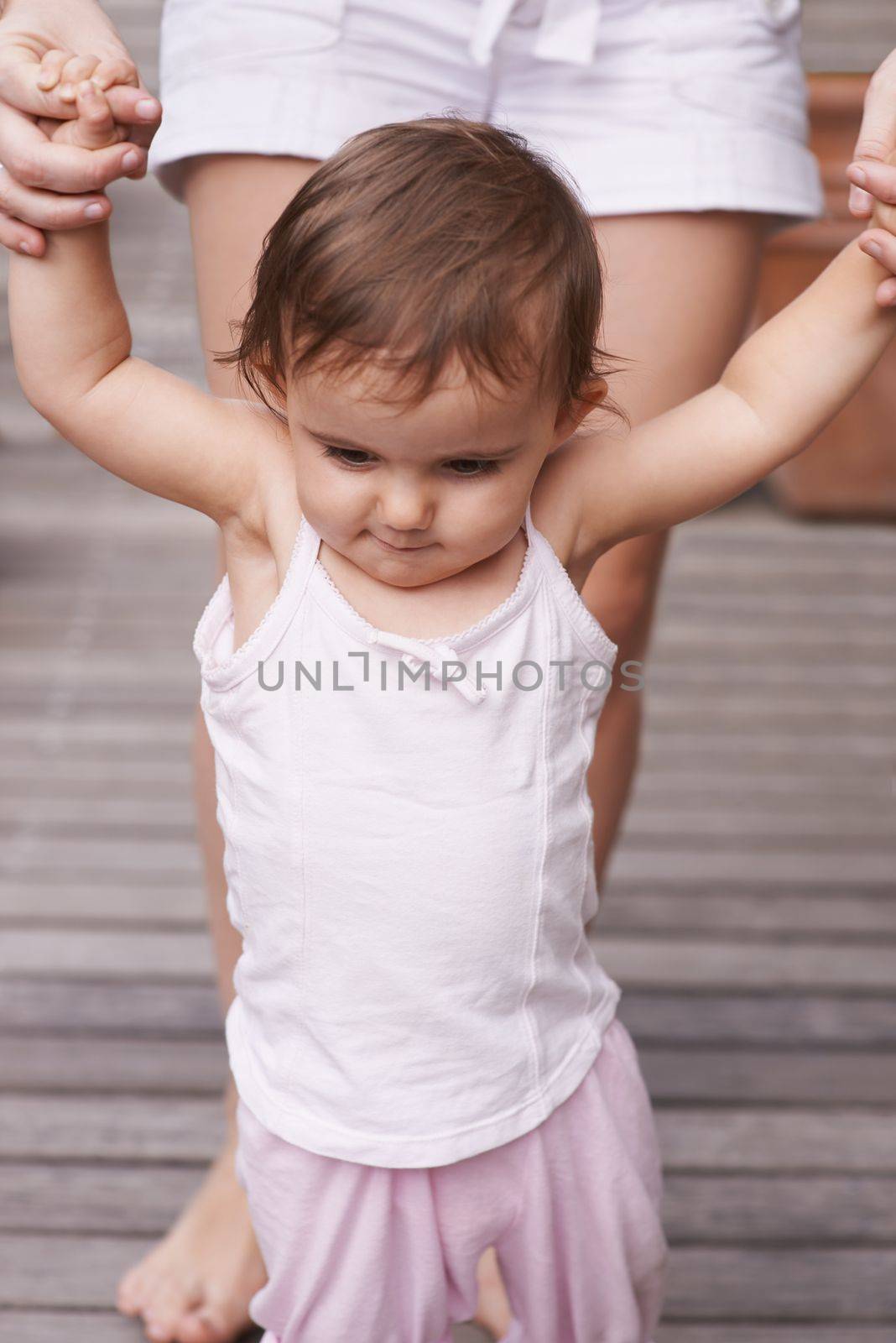 Learning to balance...a mother helping her baby daughter learn how to walk. by YuriArcurs