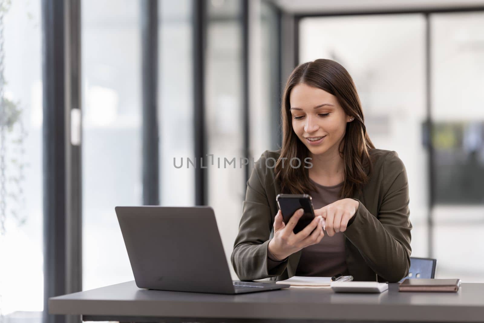 Portrait of a smiling young woman using mobile phone and laptop computer.