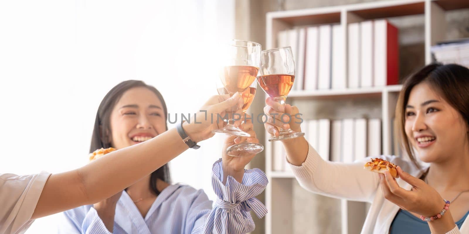 Group of Asian friends gather to celebrate Christmas with champagne and eating pizza at home. Joy of holiday party with friends or colleague concept.