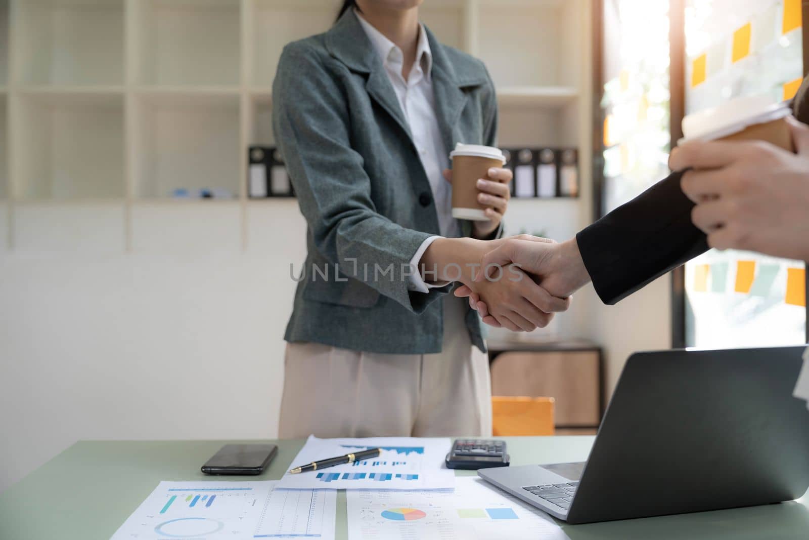 Two Asian businesswomen are shaking hands in the office. business cooperation, business dealing, Congratulations, greeting. close-up hands image.