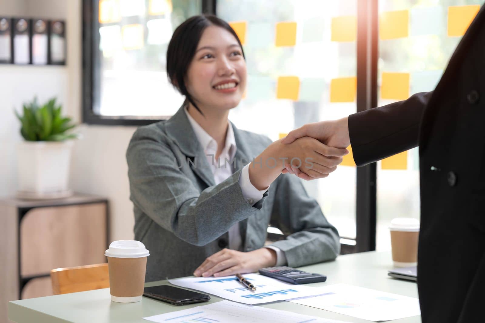 Two Asian businesswomen are shaking hands in the office. business cooperation, business dealing, Congratulations, greeting. close-up hands image by wichayada