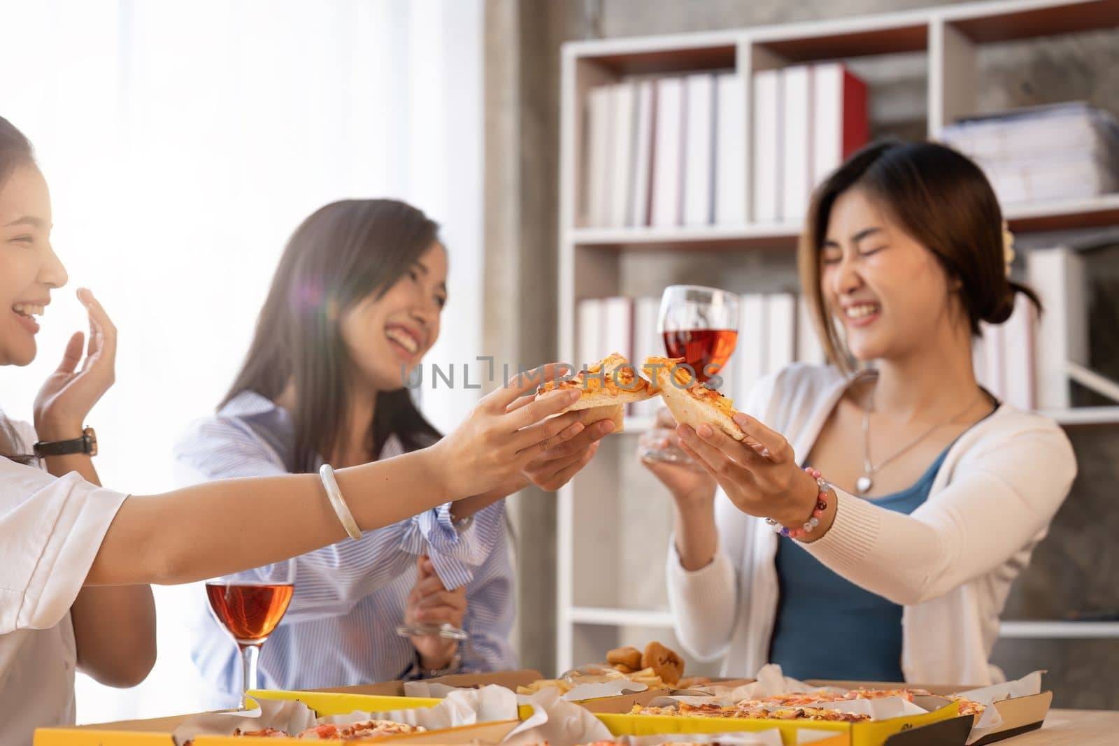 Group of Asian friends gather to celebrate Christmas with champagne and eating pizza at home. Joy of holiday party with friends or colleague concept.