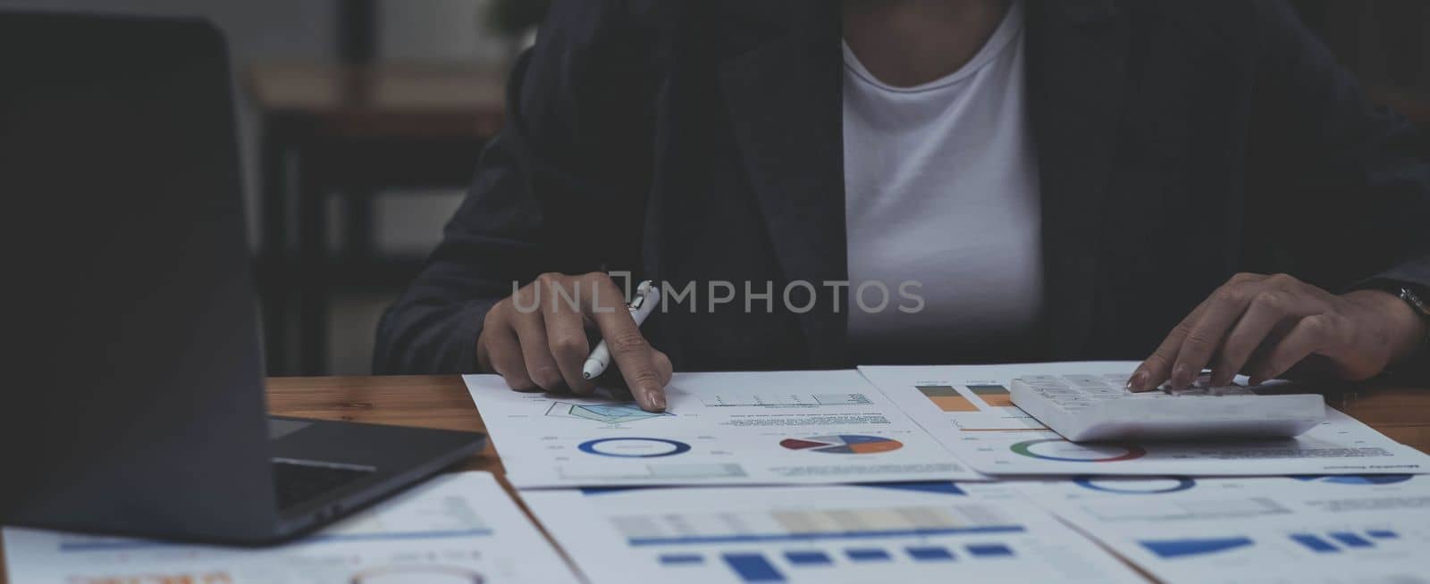 Businesswoman press the white calculator to calculate the numbers in the company financial documents, the finance department prepares the document and forwards it to be checked before the meeting..