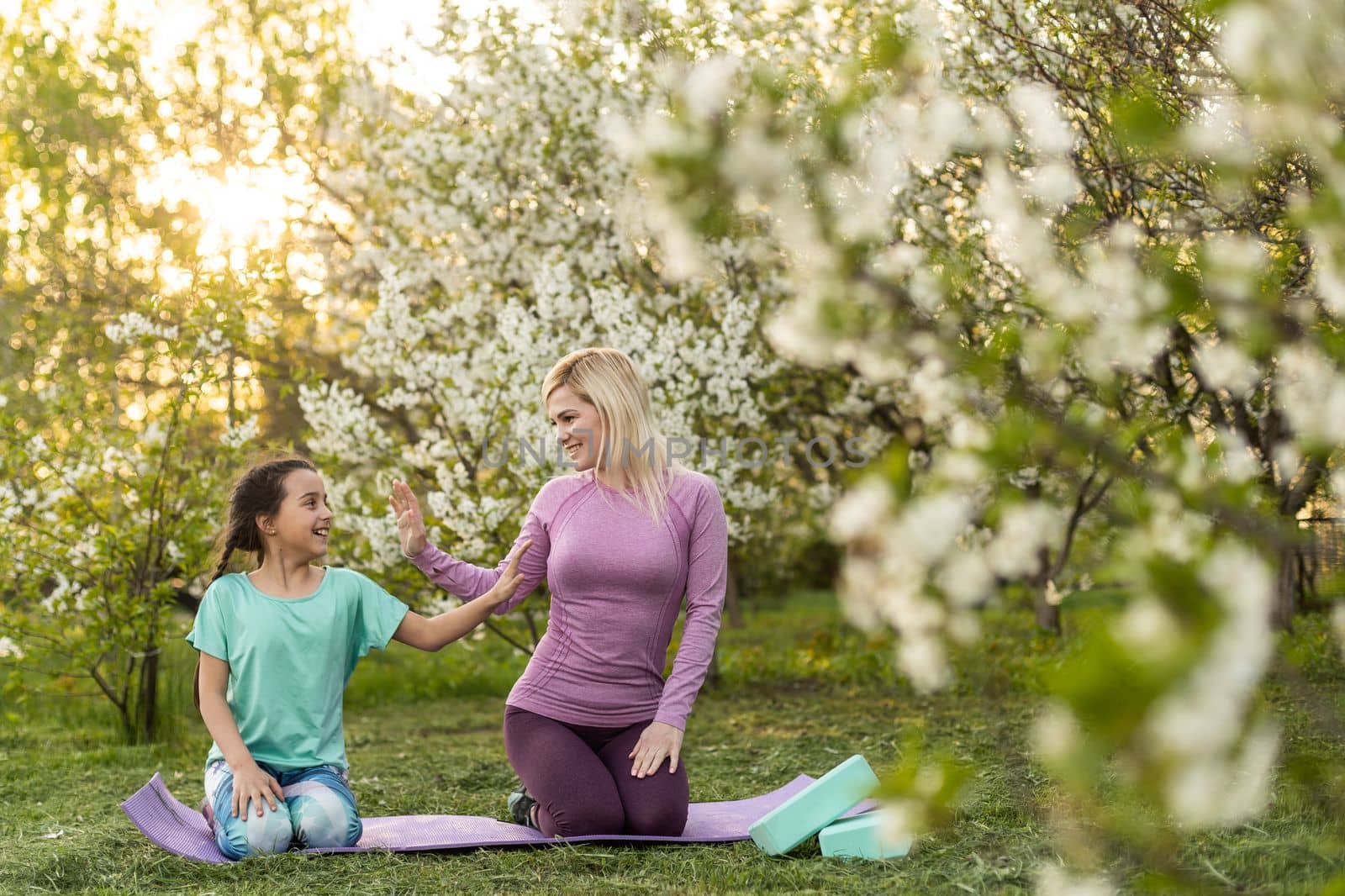 Young woman with little daughter in a sporty uniform doing yoga of a house by the garden.