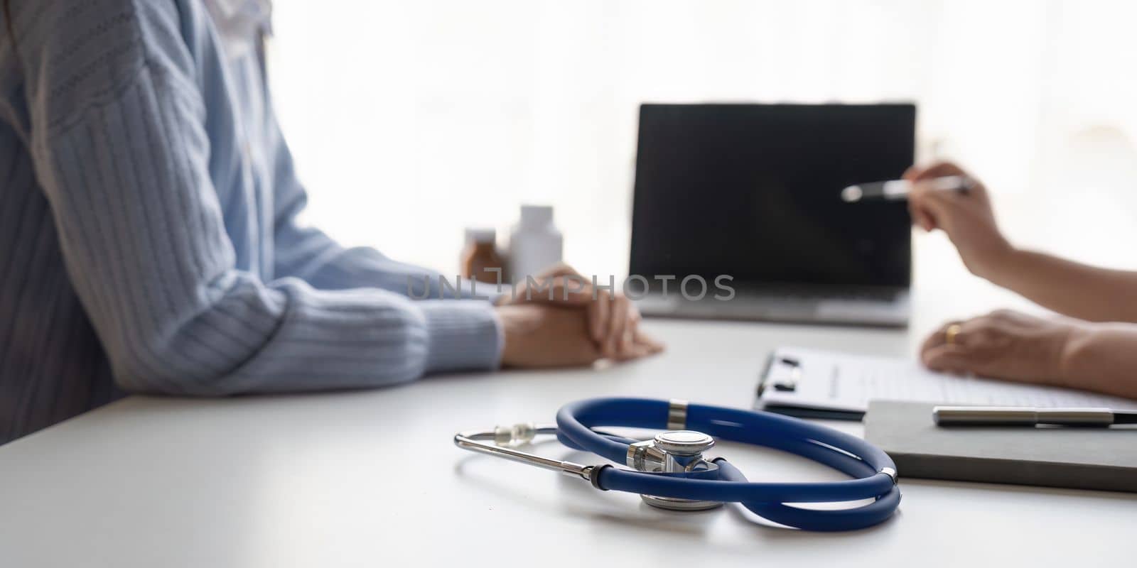 medical consultation - doctor talking to patient in clinic office on laptop computer. focus on stethoscope. by nateemee