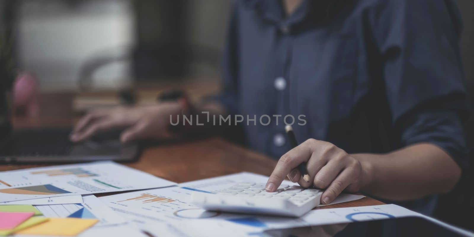 Close up of businesswoman or accountant hand holding pen working on calculator to calculate business data, accountancy document and laptop computer at office, business concept by wichayada