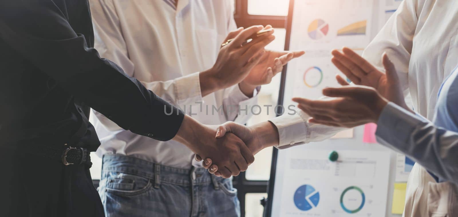 Welcome on board handsome men shaking hands with smile while sitting on the couch at office with their coworkers by wichayada