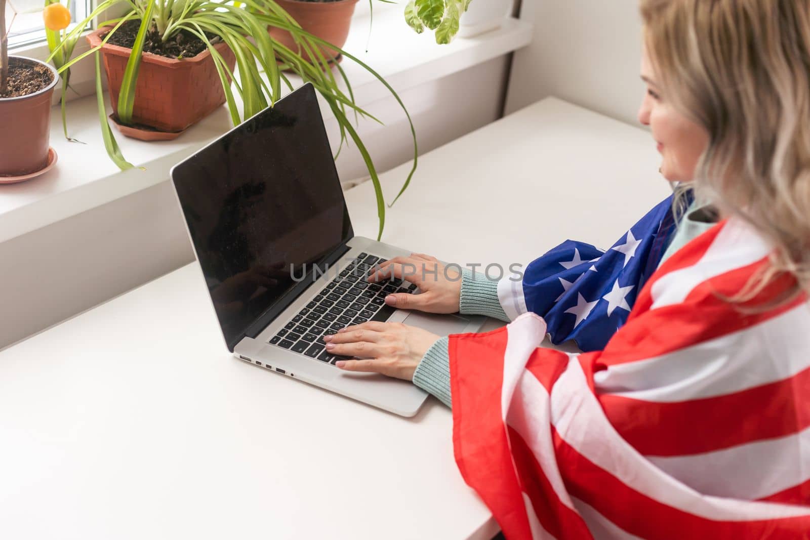 Happy woman employee sitting wrapped in USA flag, shouting for joy in office workplace, celebrating labor day or US Independence day. by Andelov13