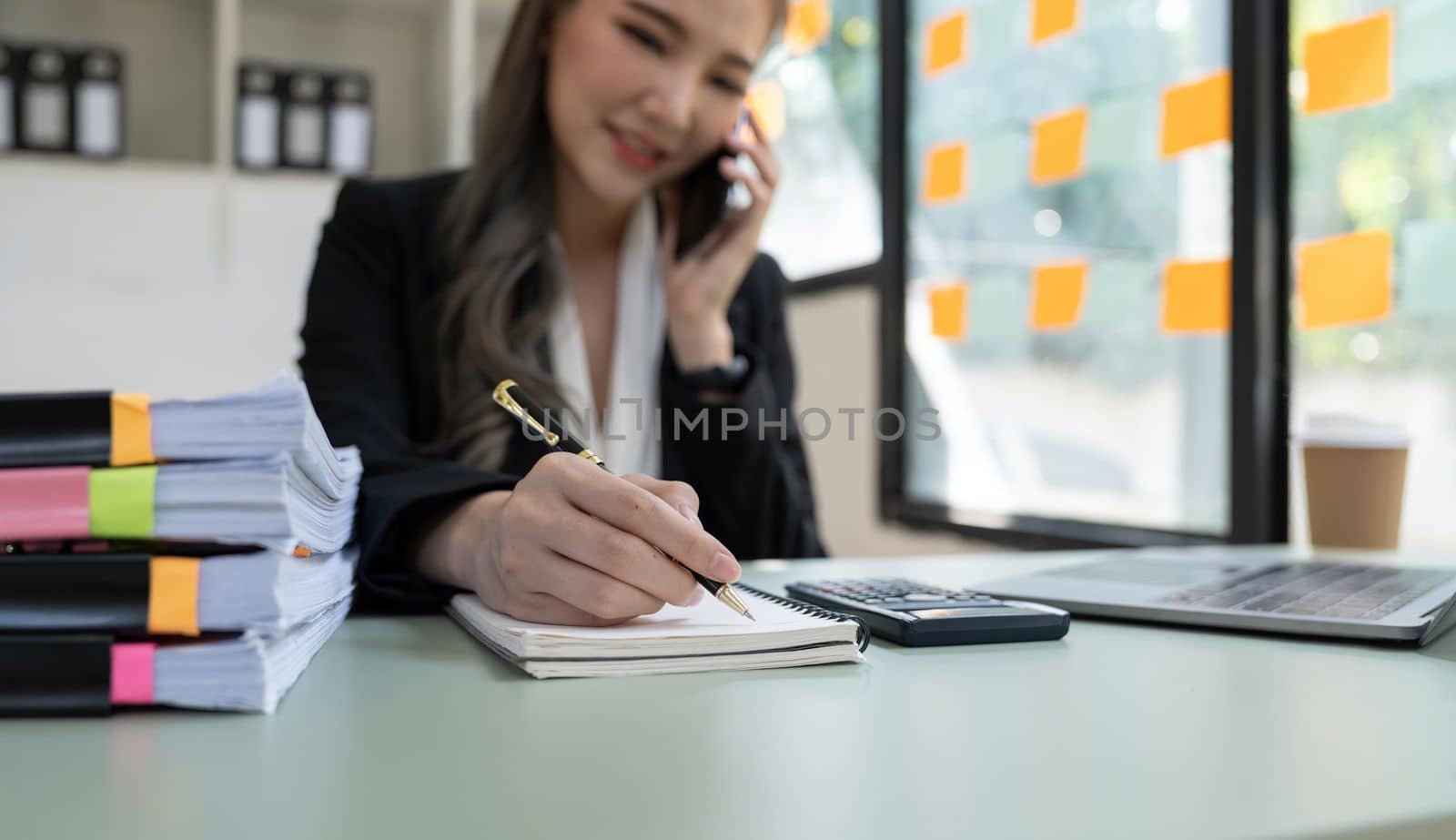 Close up business accountant asian woman calling on phone and taking notes by nateemee