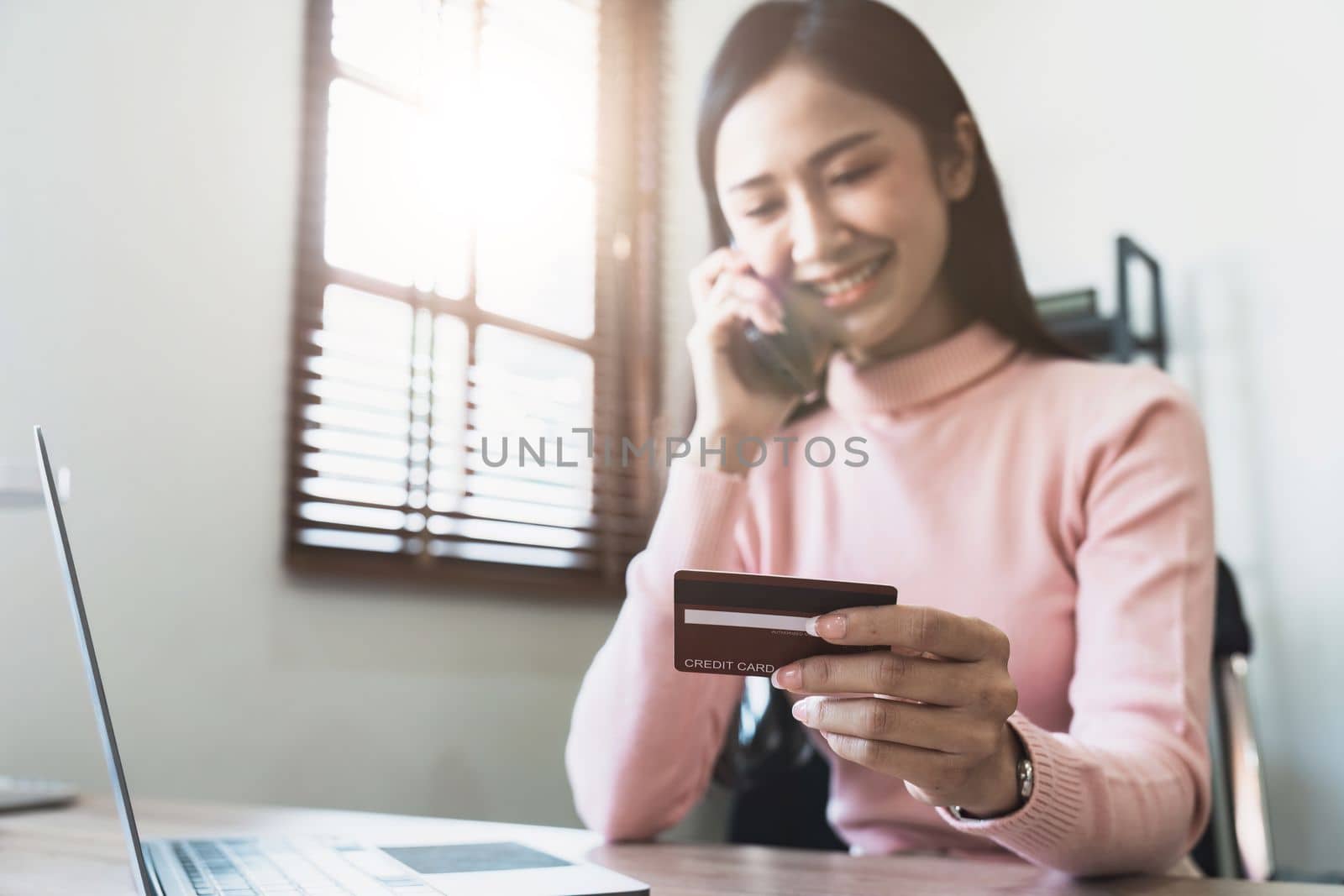Woman holding credit card and confirm purchase via telephone call to customer service, smiling asian girl making payment via smartphone conversation at home. by nateemee