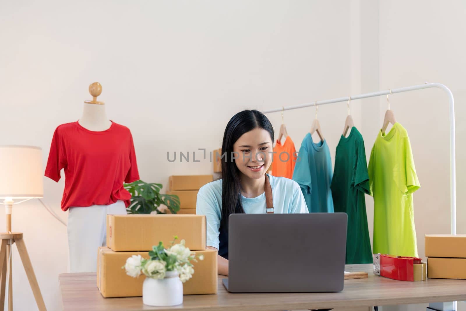 Young successful asian woman doing clothing business by open shop and selling online. she using laptop computer. online sell marketing delivery, SME e-commerce telemarketing concept.