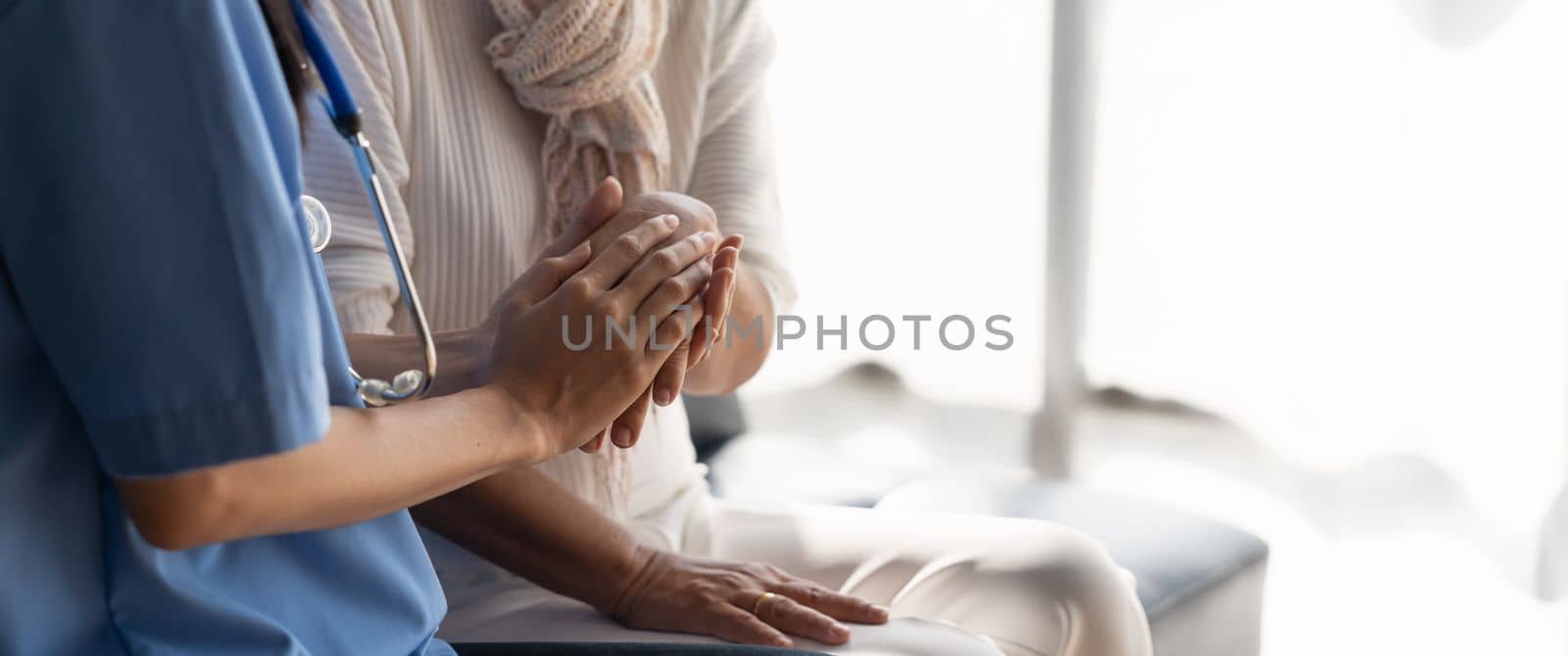 Happy patient is holding caregiver for a hand while spending time together. Elderly woman in nursing home and nurse