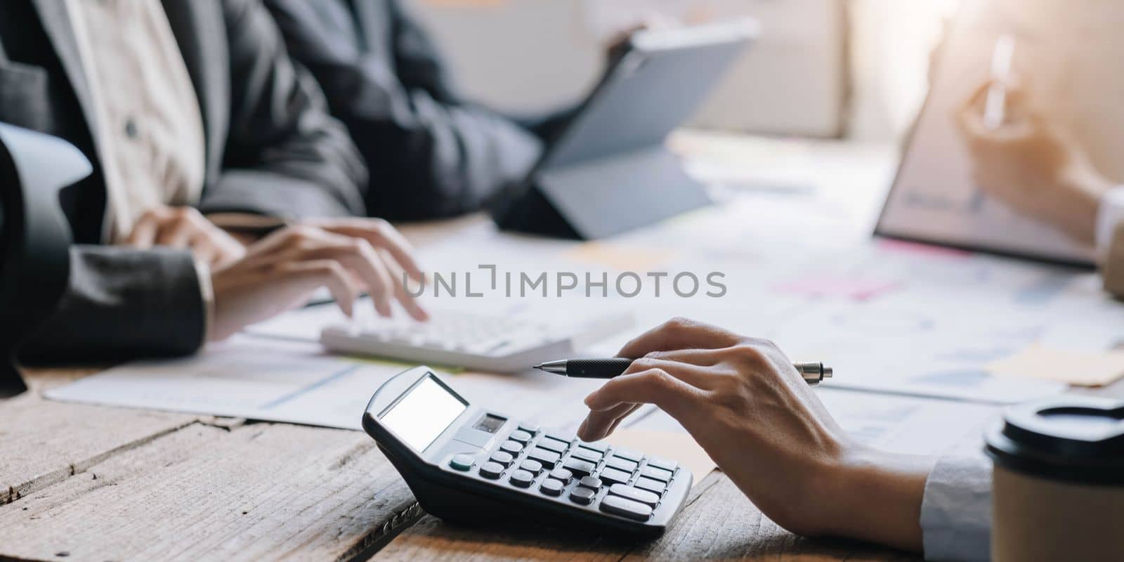 Accountant or bookkeeper working with calculator to calculate business data summary report, accountancy document and laptop computer at office, business meeting concept by wichayada