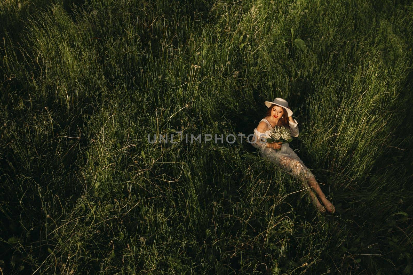 Portrait of a beautiful woman in a white dress and a hat with lilies of the valley. A girl in nature. Spring flowers.