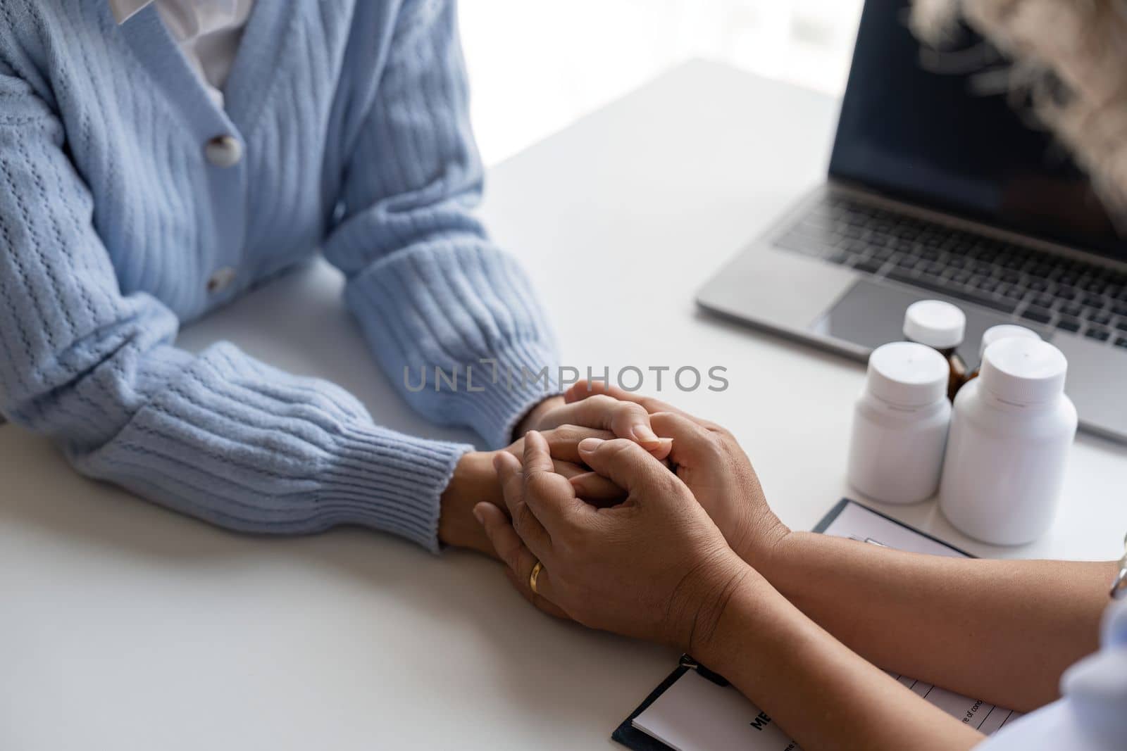 Doctor giving hope. Close up shot of young female physician leaning forward to smiling elderly lady patient holding her hand in palms. Woman caretaker in white coat supporting encouraging old person.