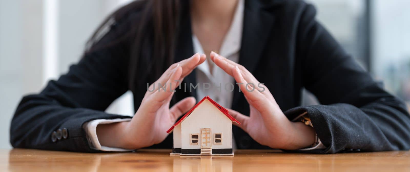 Wooden toy house protected by hands. Home insurance concept. banner ratio.