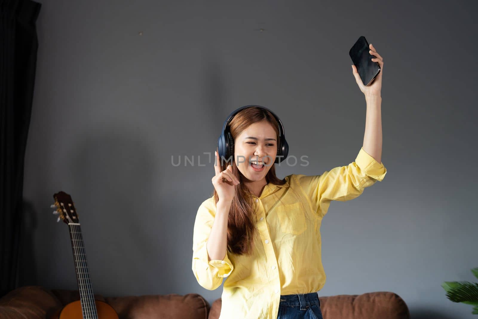 Happy woman listening music through wireless headphones standing on sofa at home