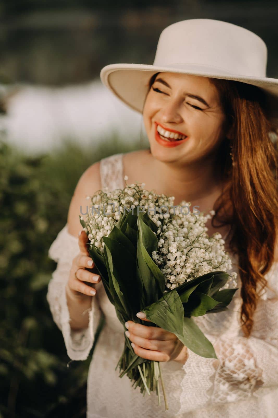 Portrait of a beautiful woman in a white dress and a hat with lilies of the valley. A girl in nature. Spring flowers.