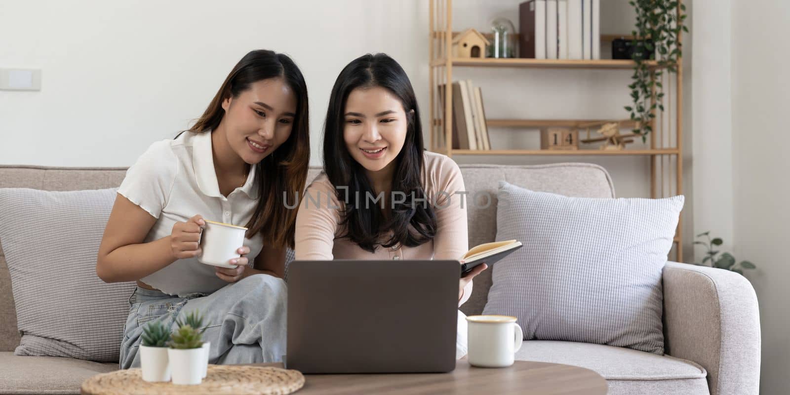 Happy young asian women LGBT lesbian happy couple sitting on sofa using laptop a computer in living room at home. LGBT lesbian couple together by nateemee
