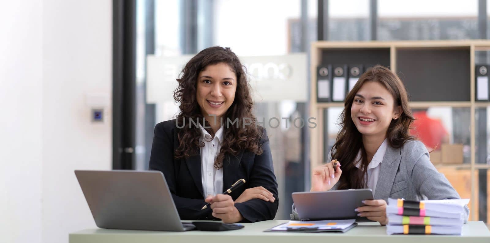 Two young Asian business woman talk, consult, discuss working with new startup project idea presentation analyze plan marketing and investment in the office. by wichayada