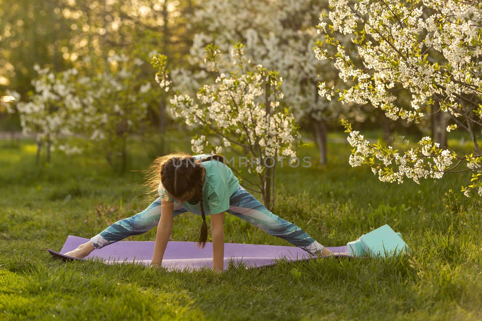 a little girl does yoga lying on a sports mat in the park. a healthy lifestyle is a childish habit by Andelov13