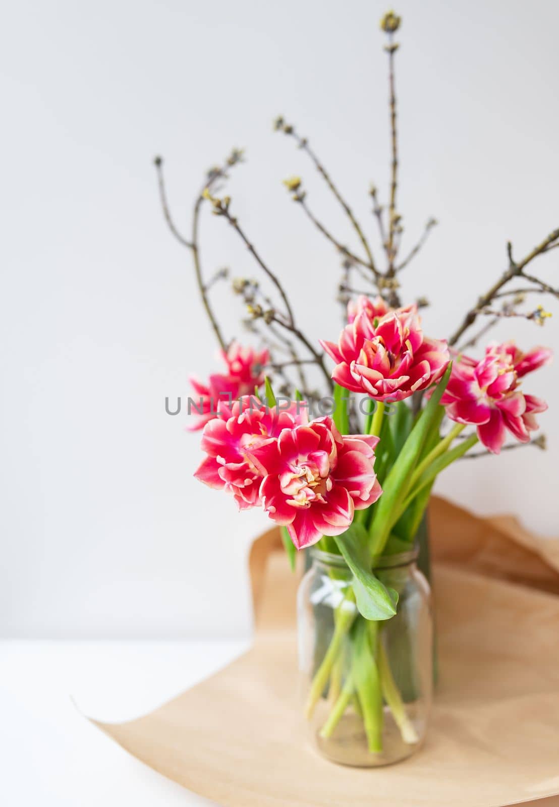 A beautiful spring bouquet of tulips stands in a vase along with spring branches. Surprise concept, birthday. Vertical photo, place for an inscription