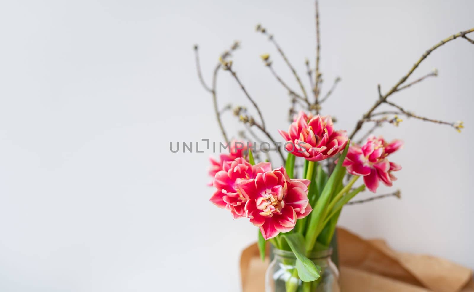 A beautiful spring bouquet of tulips stands in a vase along with spring branches. Surprise concept, birthday. Place for an inscription