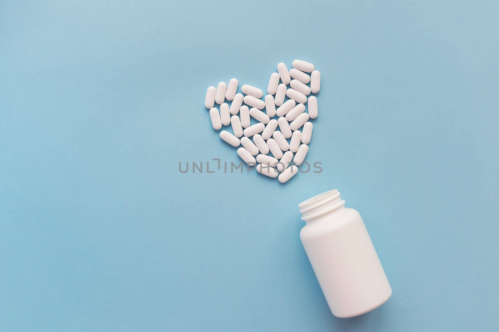 White pills in the shape of a heart and a white jar on a blue background. Pills for heart health. The concept of medicine and health care
