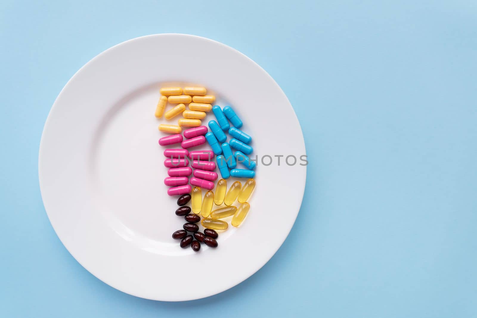 White plate with pills of nutritional supplements in different bright colors. Blue background, place for an inscription