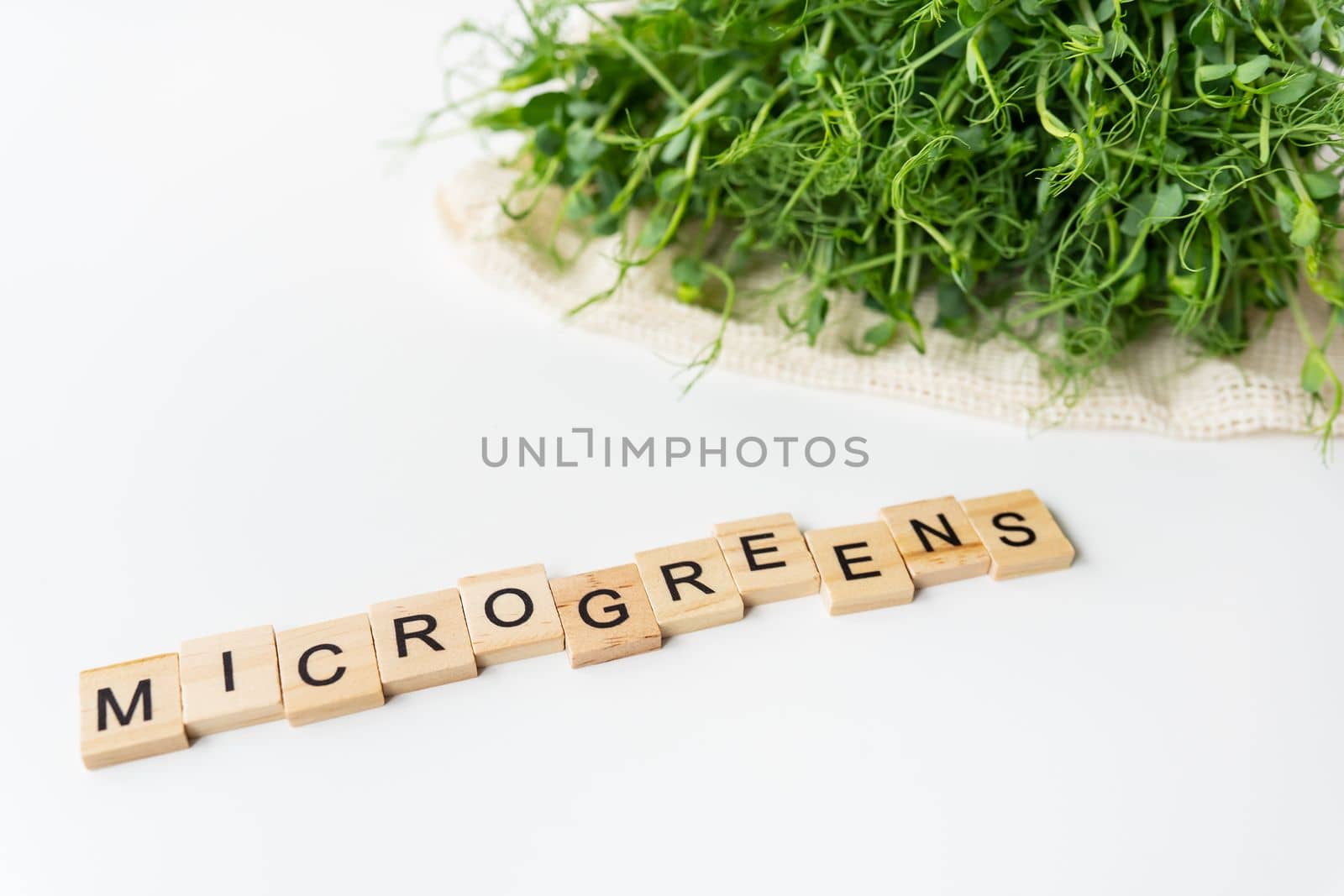 Vegetable pea sprouts, microgreens on white background, vegan health superfood. Inscription from wood letters microgreen