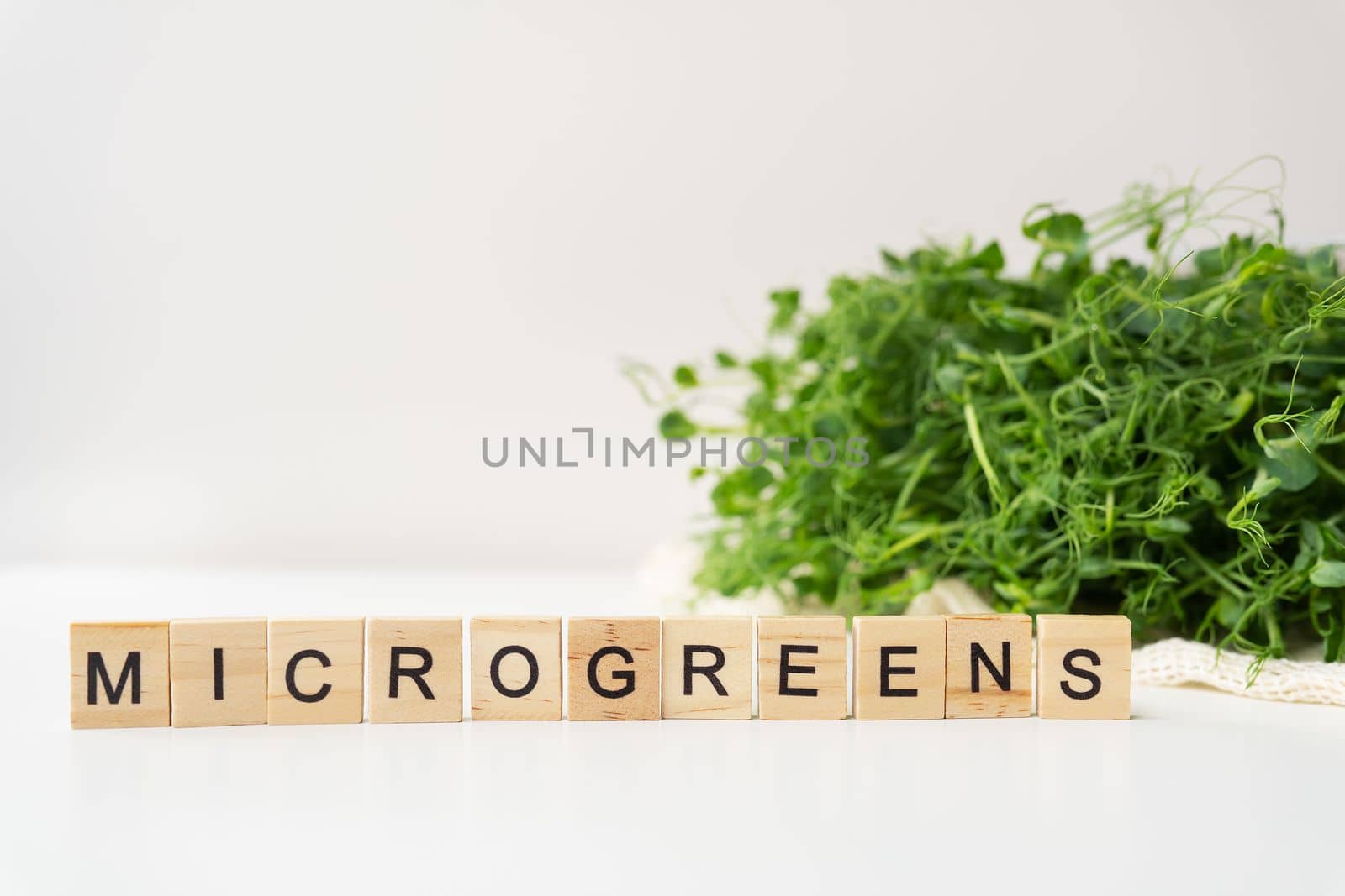 Vegetable pea sprouts, microgreens on white background, vegan health superfood. Inscription from wood letters microgreen