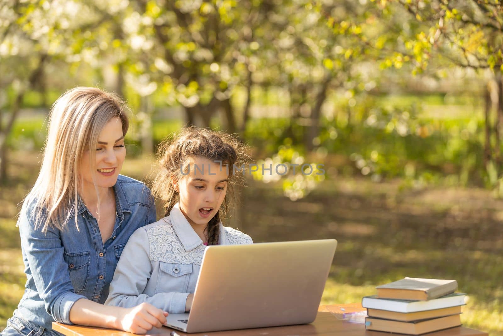 Beautiful mom with little daughter resting with a laptop in the park on a sunny day. Study, Learning, harmony, happiness, paradise - concept.