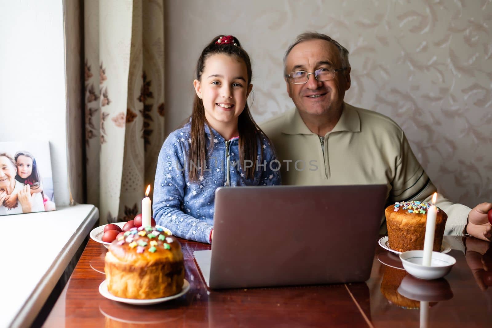 grandfather and granddaughter using laptop on kitchen, online, video call to friends, easter at home during coronavirus covid-19 outbreak