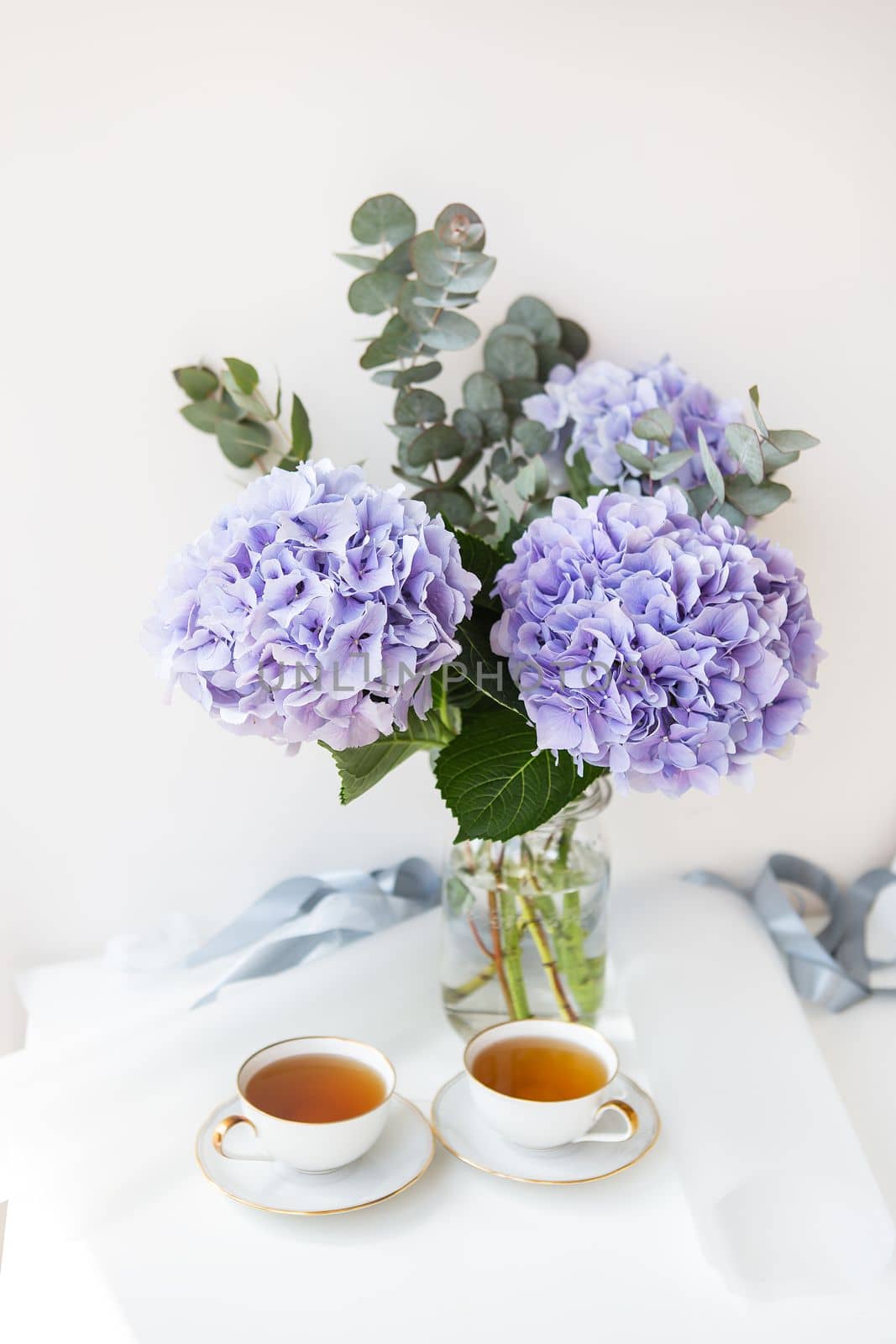 Two cups of black tea in a porcelain beautiful white cup with a gold cut. Beautiful bouquet of purple hydrangea on the table. Tea break