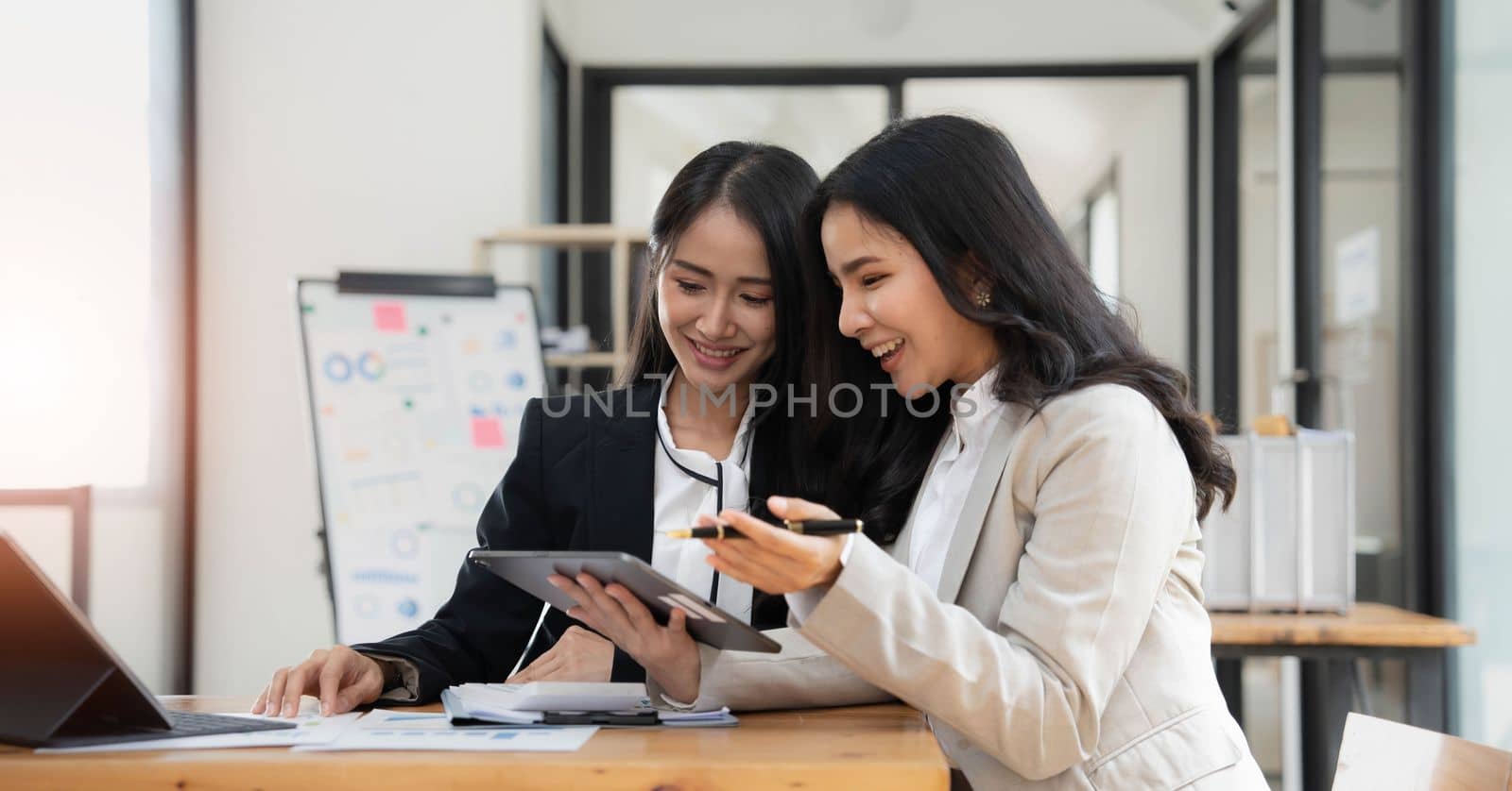 Two young Asian businesswoman discuss investment project working and planning strategy. Business people talking together with laptop computer at office. by wichayada