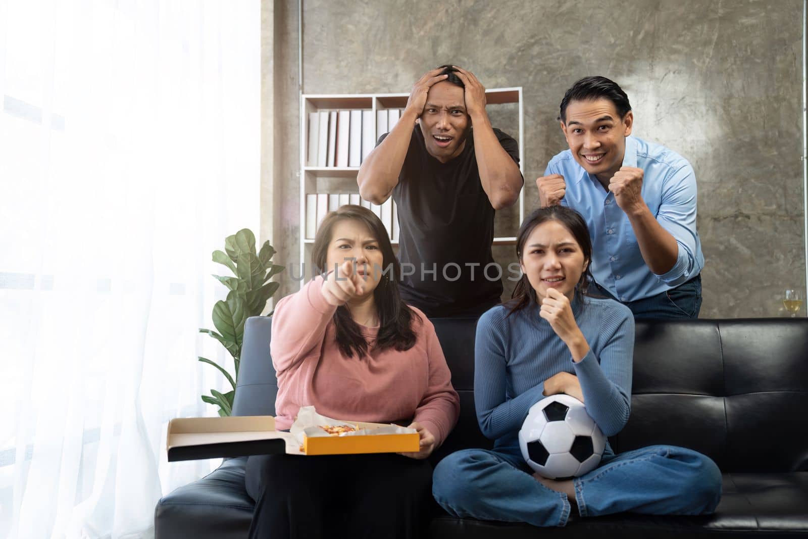 Friends watch sports on TV, cheer and celebrate. Happy diverse asian friend supporters fans sit on couch with popcorn and drinks.