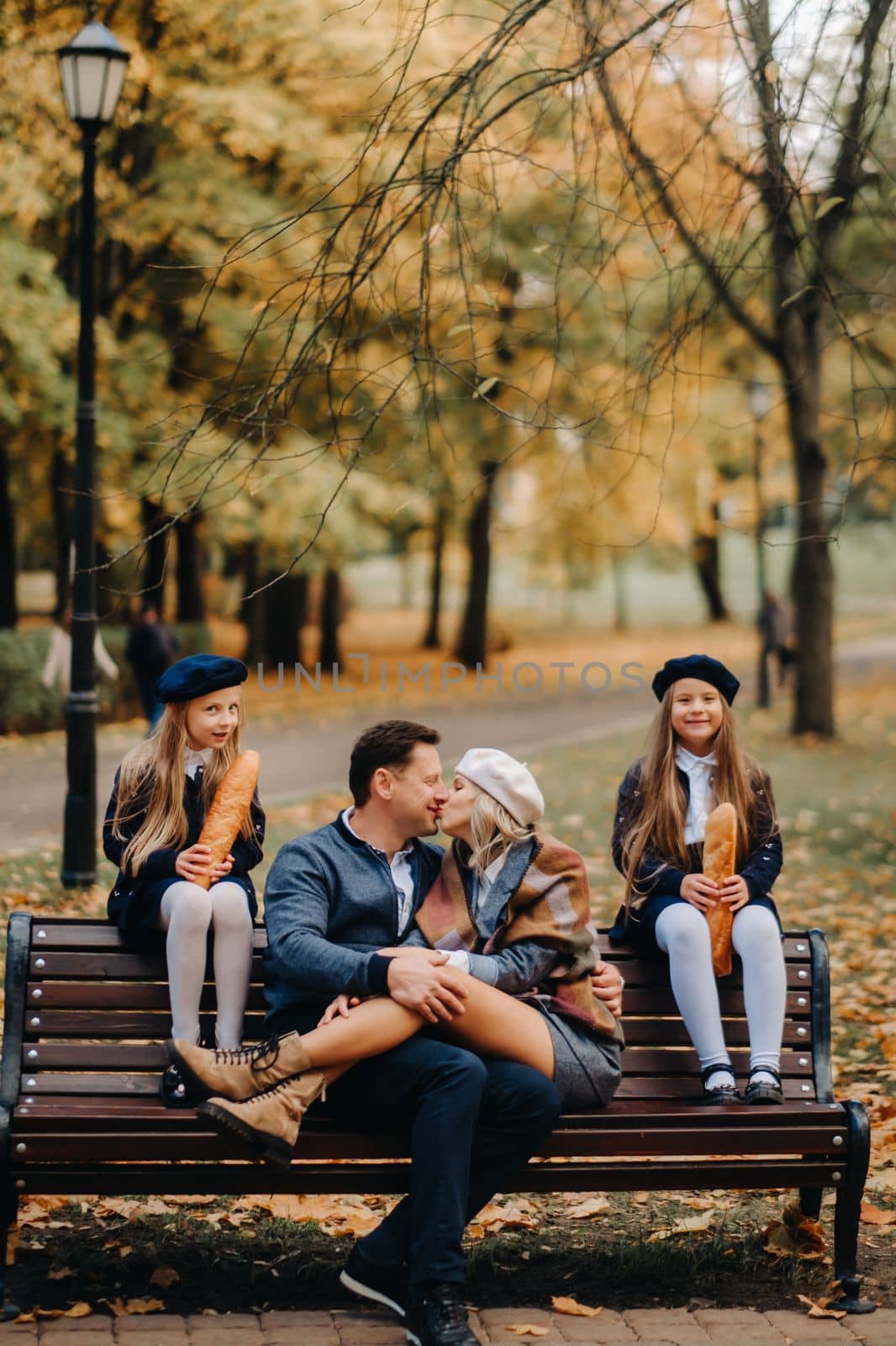 A large family is sitting on a bench in an autumn park. Happy people in the autumn park by Lobachad