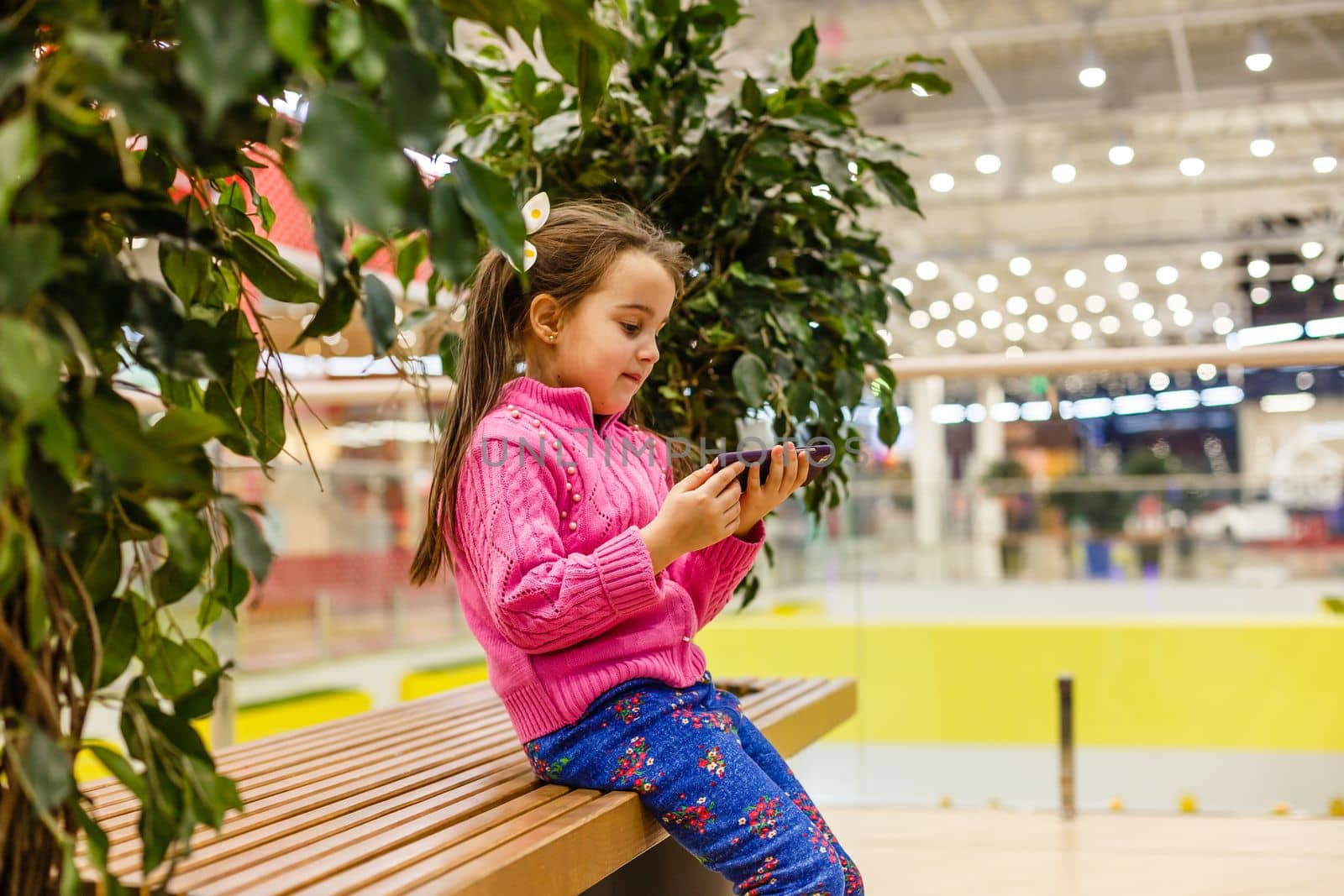 Little child girl playing with smartphone in modern commercial supermarket center
