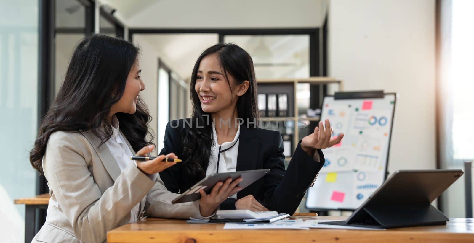 Two young Asian businesswoman discuss investment project working and planning strategy. Business people talking together with laptop computer at office. by wichayada