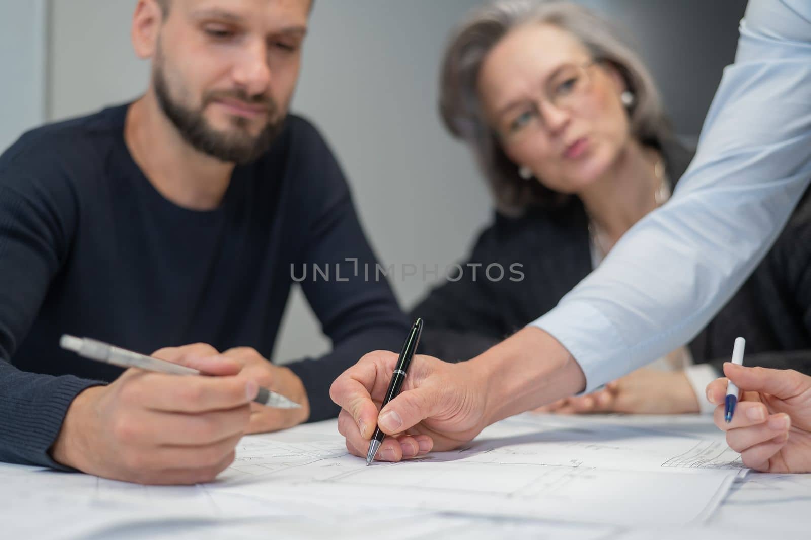 Four colleagues are discussing blueprints in a conference room in an office. Brainstorming of engineers and architects