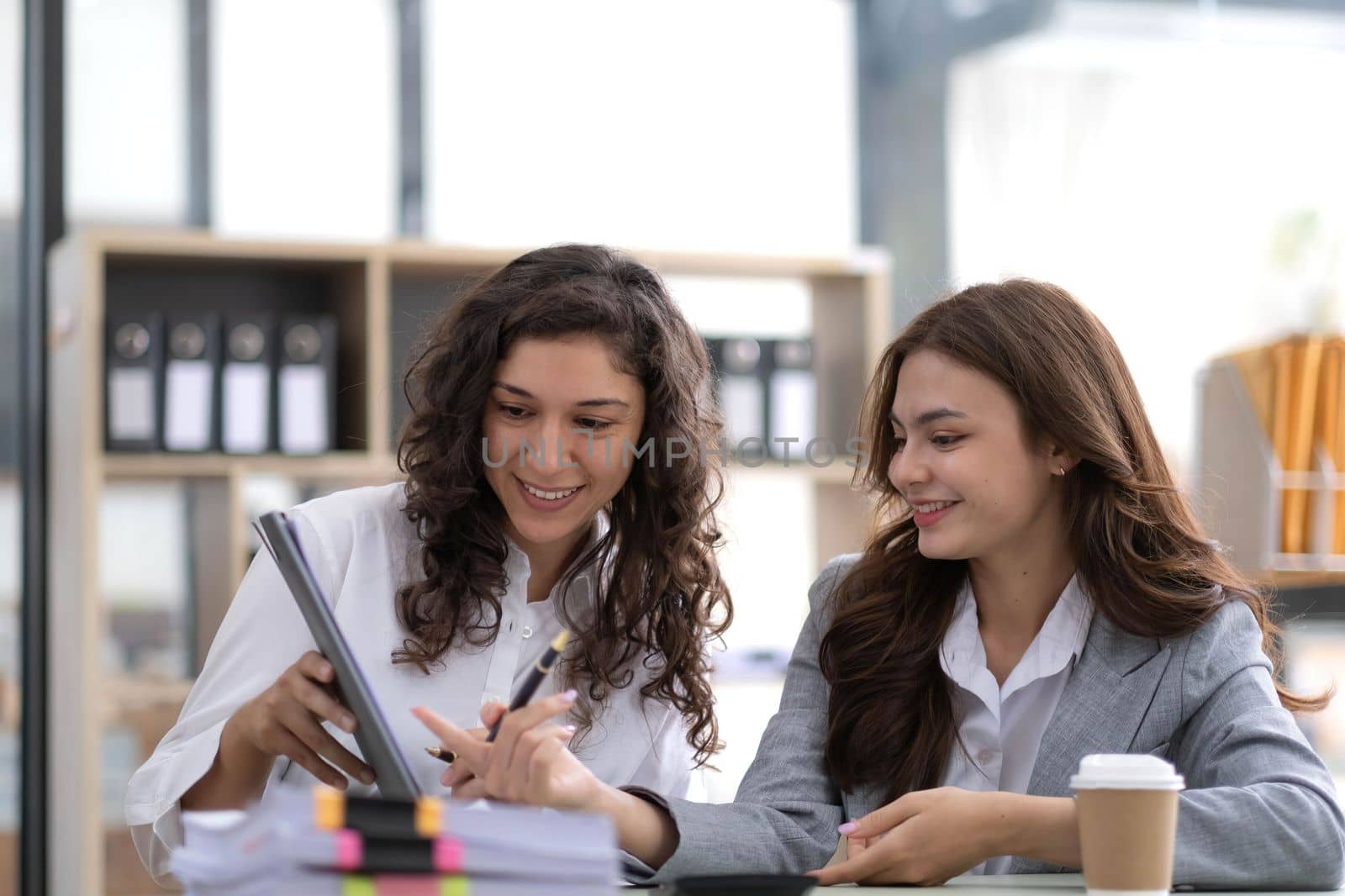 Two young Asian business woman talk, consult, discuss working with new startup project idea presentation analyze plan marketing and investment in the office..