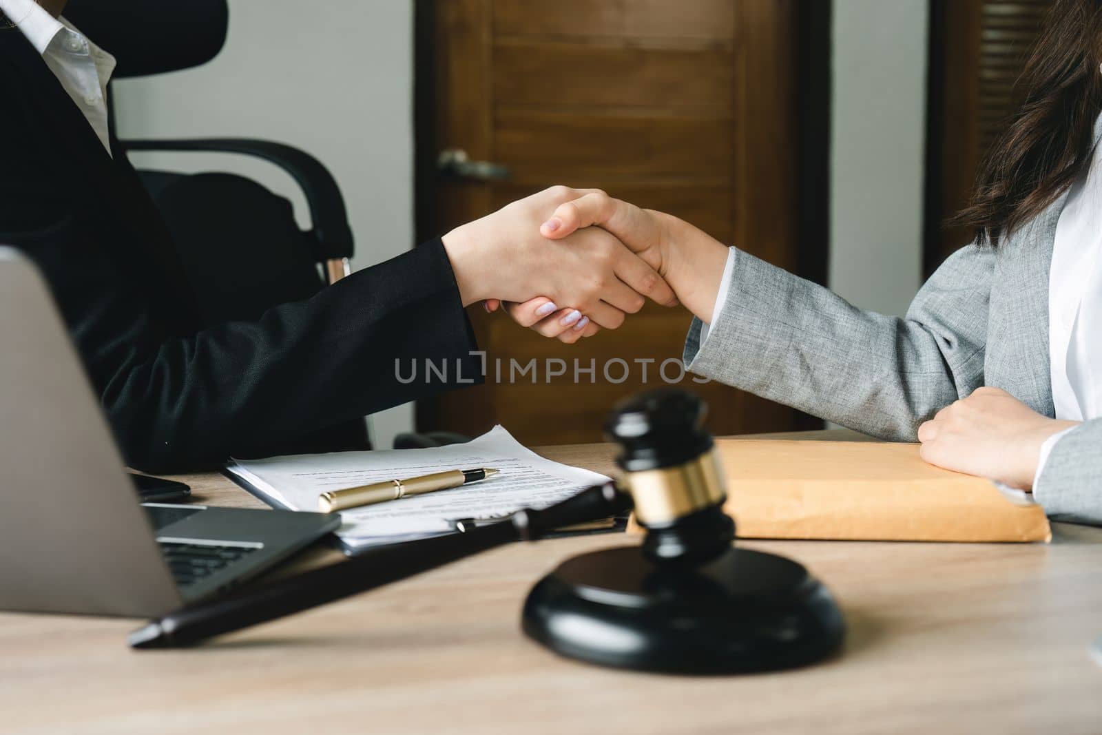 Gavel Justice hammer on wooden table with judge and client shaking hands after adviced in background at courtroom, lawyer service concept.