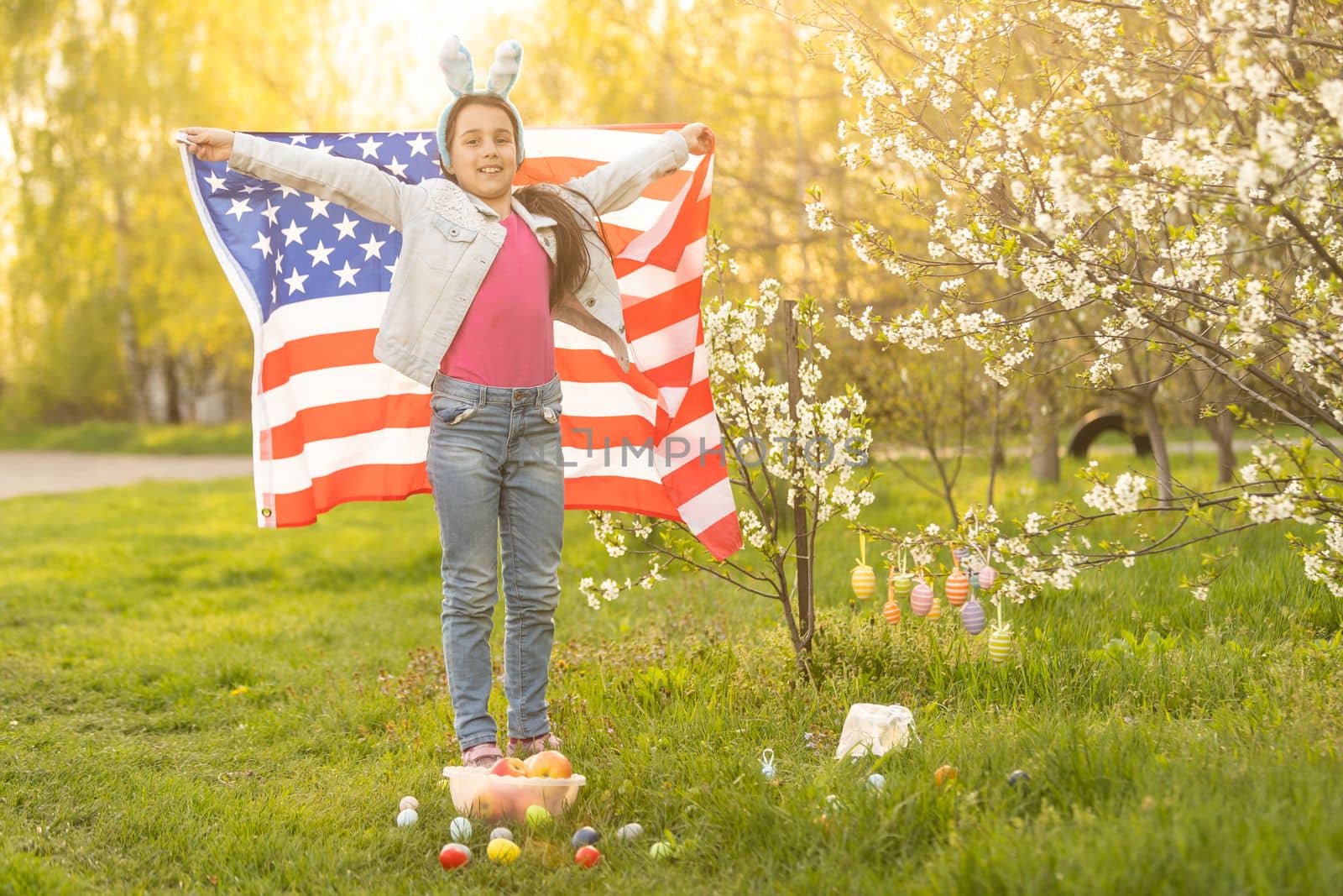 Girl kid in rabbit bunny ears on head with colored eggs and american flag. easter.