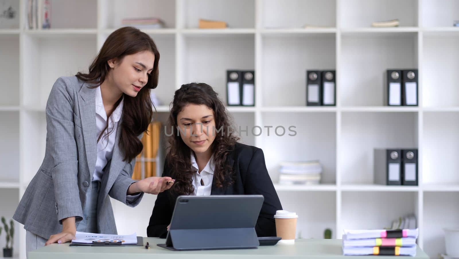 Two young Asian business woman talk, consult, discuss working with new startup project idea presentation analyze plan marketing and investment in the office. by wichayada