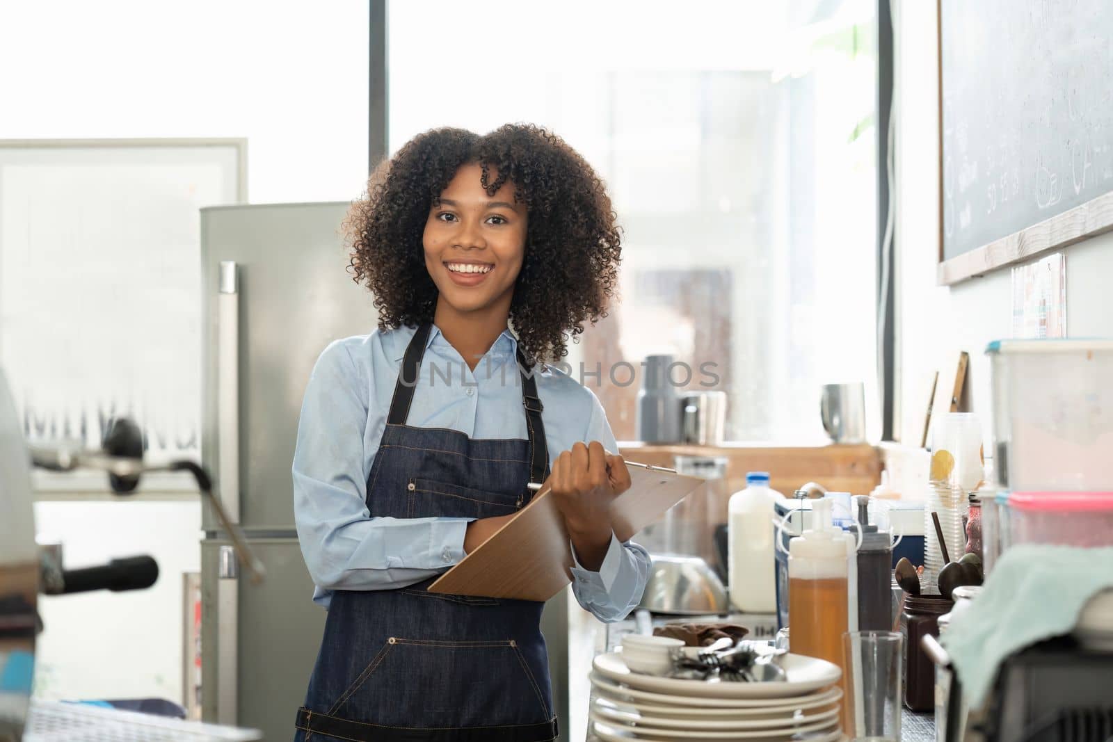 Portrait of a smiling young african american waitress wearing apron ready to take customer order by nateemee