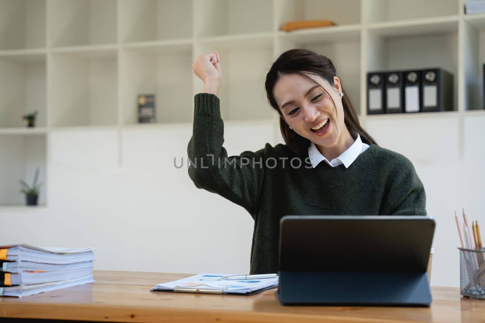 Portrait of happy young business woman celebrating success with arms up in front of laptop. Asian female won a lot of money in lottery prize, raised arms with fists. Freelancer finished project
