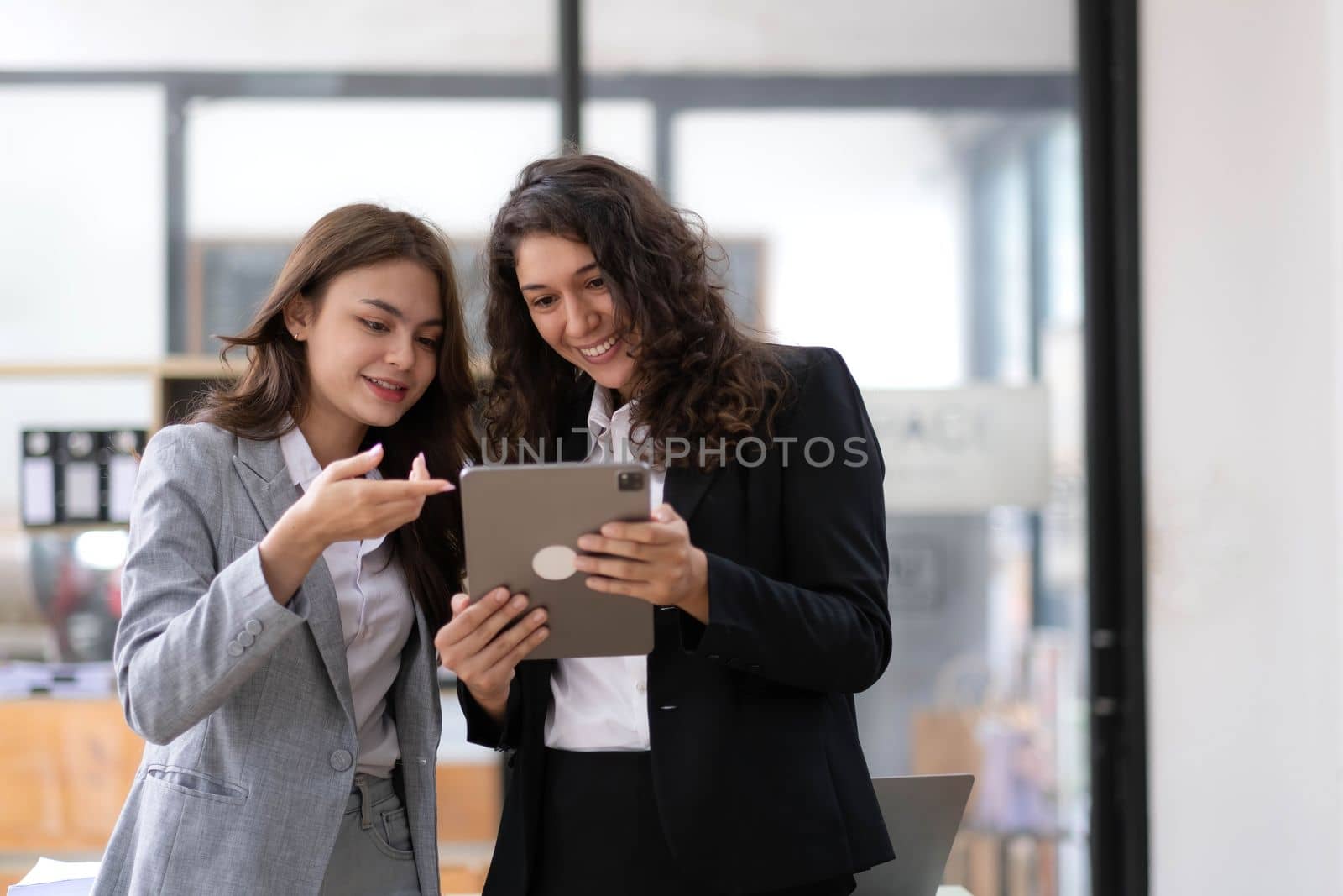 Two beautiful Asian businesswomen standing using digital tablet consulting and analyzing information in office work..